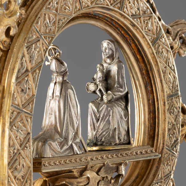 In die Krümme des Bischofsstabes ist eine figürliche Szene eingebettet, die einen knienden Bischof vor einer thronenden Gottesmutter mit Kind zeigt.