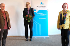 Christiane Hölscher neue Stiftungsratsvorsitzende der Schulstiftung: Zwei Frauen und ein Mann stehen in einem raum, dahinter das Logo der Schulstiftung. 